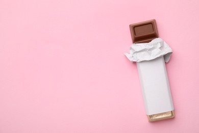 Photo of Tasty chocolate bar in package on pink background, top view. Space for text