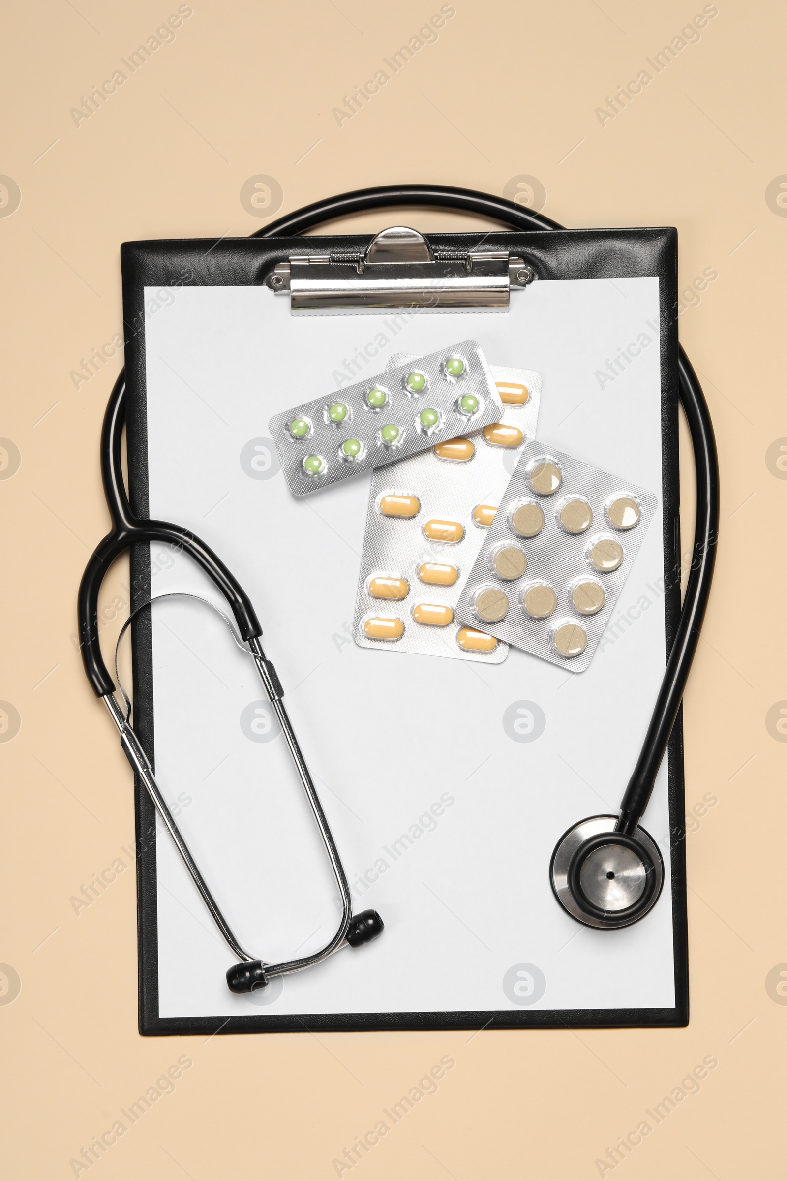 Photo of Stethoscope, pills and clipboard on beige background, top view. Medical tool