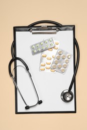 Stethoscope, pills and clipboard on beige background, top view. Medical tool