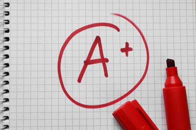 Photo of School grade. Red letter A with plus symbol on notebook paper and marker, top view