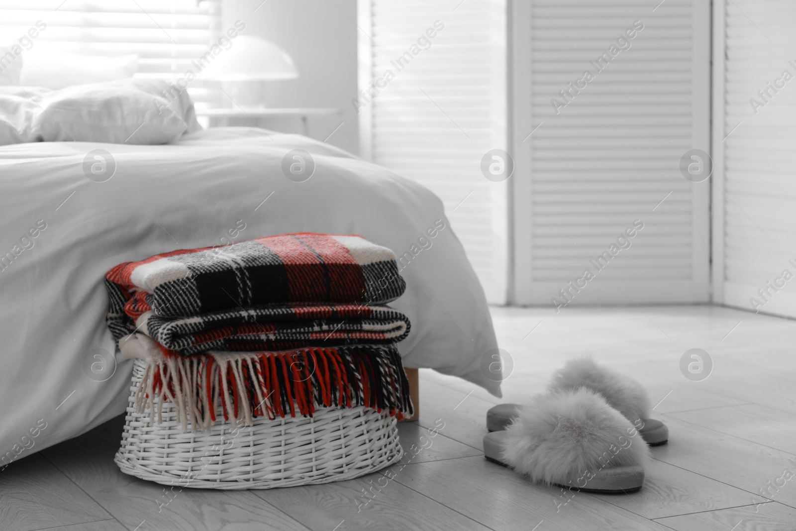 Photo of Folded warm checkered plaid on wicker basket near bed indoors
