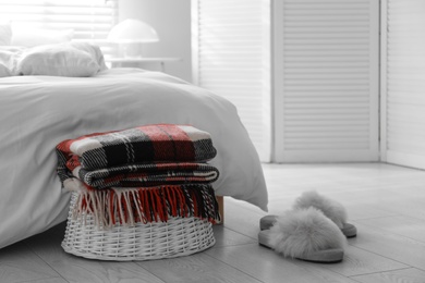 Folded warm checkered plaid on wicker basket near bed indoors