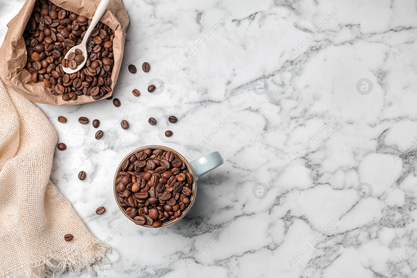 Photo of Ceramic cup and paper bag with coffee beans on marble background, top view