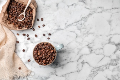 Photo of Ceramic cup and paper bag with coffee beans on marble background, top view