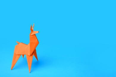 Photo of Origami art. Handmade orange paper deer on light blue background, space for text
