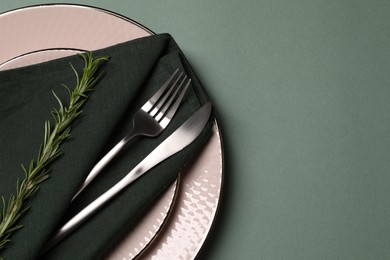 Stylish table setting. Plates, cutlery, napkin and rosemary on green background, top view with space for text