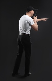 Male security guard using portable radio transmitter on dark background