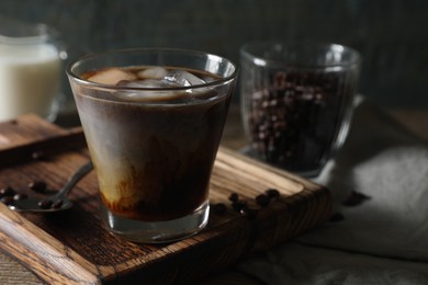 Photo of Glass of delicious iced coffee with milk and beans on wooden table, space for text