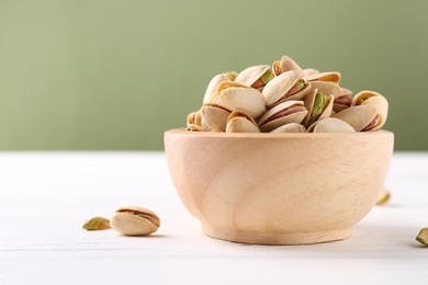 Tasty pistachios in bowl on white wooden table against olive background, closeup. Space for text