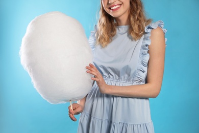 Young woman with tasty cotton candy on blue background, closeup
