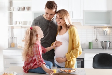 Photo of Pregnant woman and her family eating pizza in kitchen