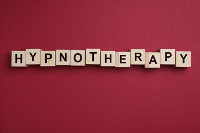 Photo of Wooden blocks with word HYPNOTHERAPY on red background, flat lay