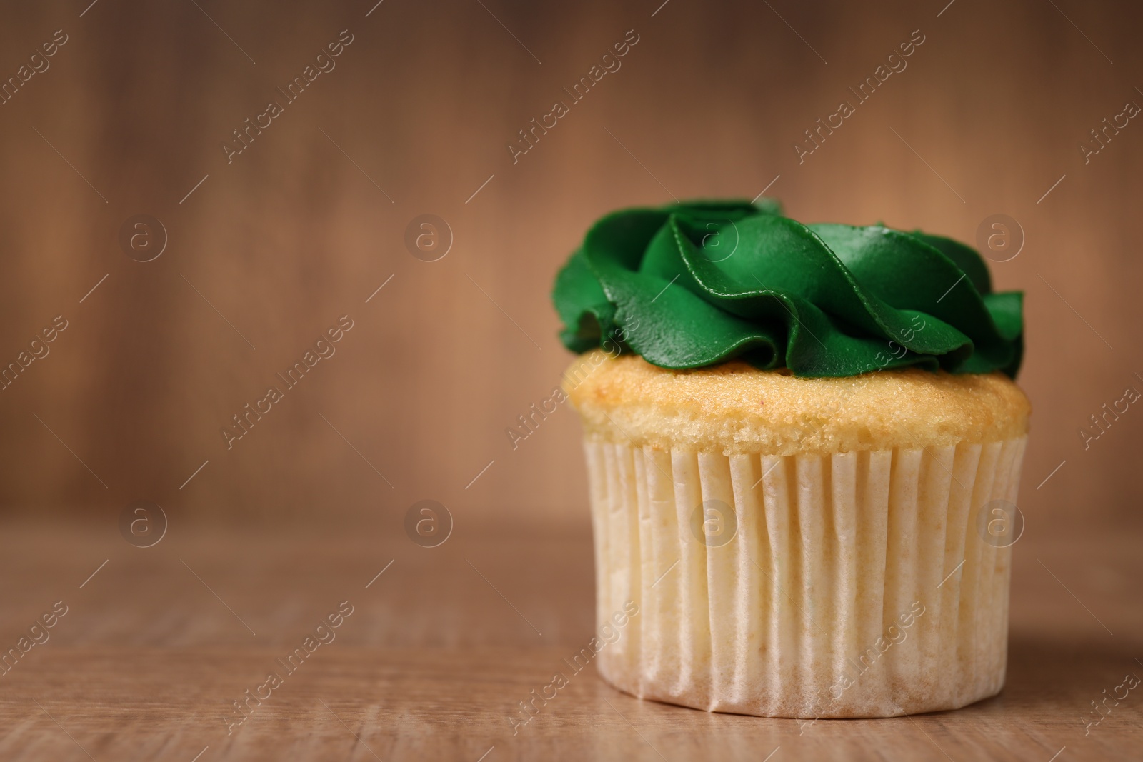 Photo of Delicious cupcake with bright cream on wooden table, closeup. Space for text