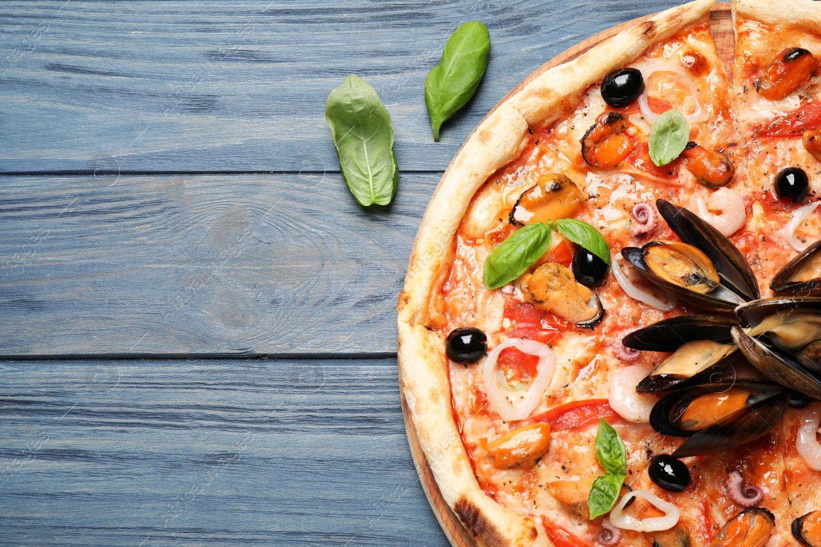 Photo of Tasty pizza with seafood and fresh basil on blue wooden table, flat lay. Space for text