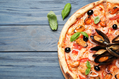 Photo of Tasty pizza with seafood and fresh basil on blue wooden table, flat lay. Space for text