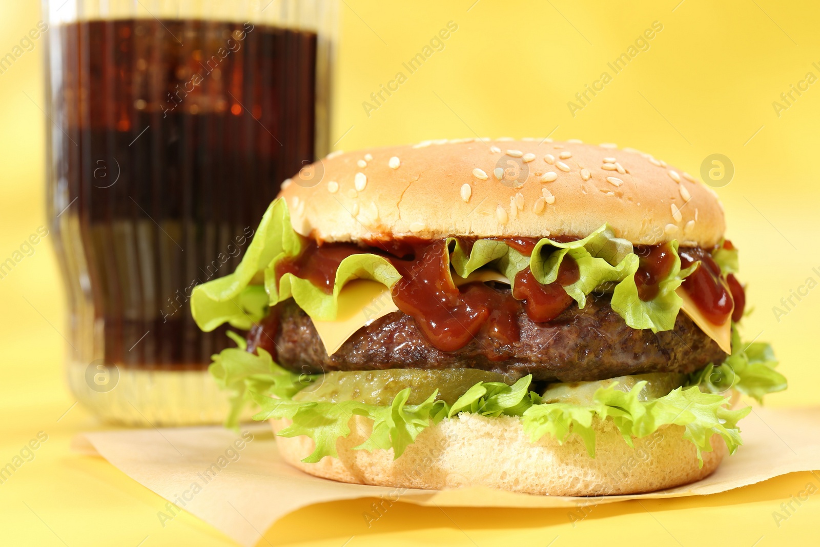 Photo of Burger with delicious patty and soda drink on yellow background, closeup