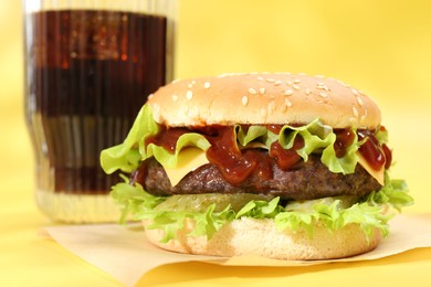 Photo of Burger with delicious patty and soda drink on yellow background, closeup