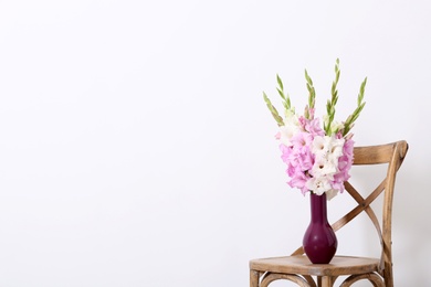 Photo of Vase with beautiful gladiolus flowers on wooden chair against white background