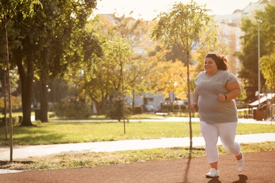 Beautiful overweight woman running in park on sunny day