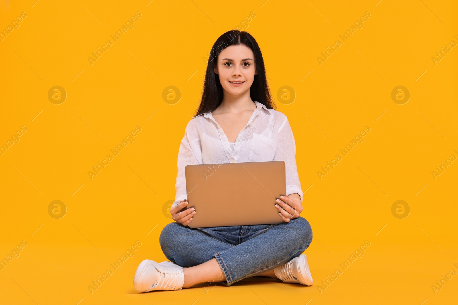 Photo of Smiling student with laptop sitting on yellow background