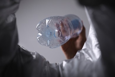 Bottom view of woman throwing plastic bottle into trash bin on grey background, closeup