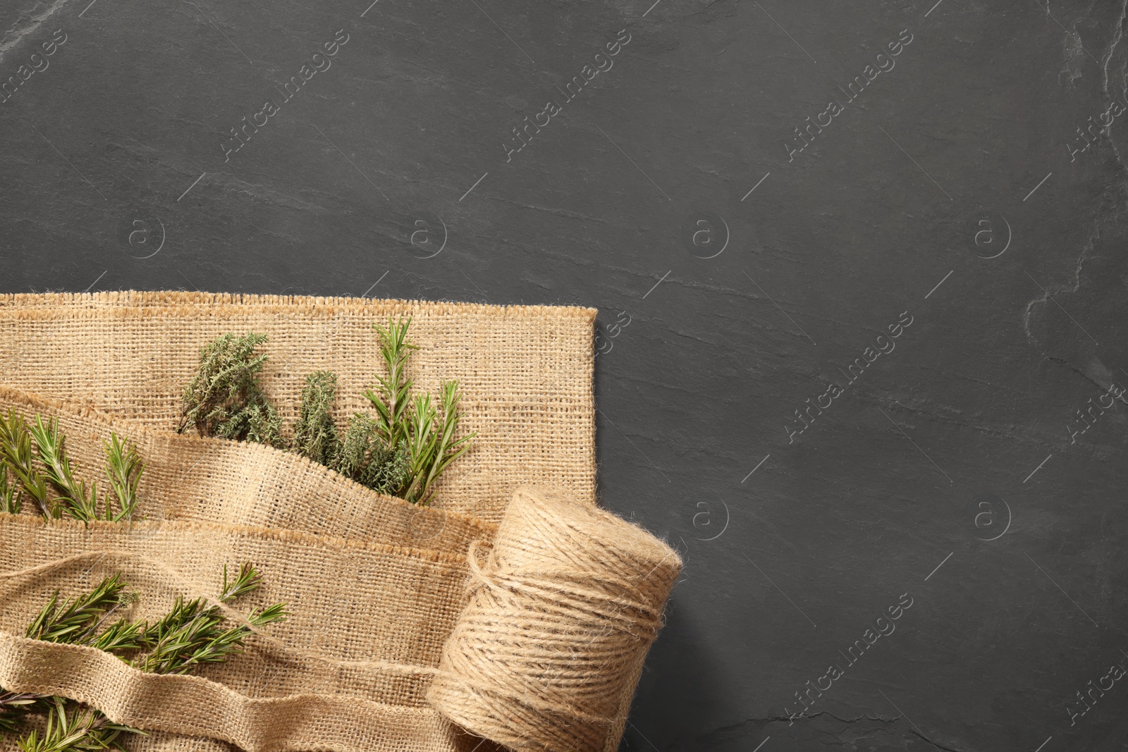 Photo of Natural burlap fabric, jute and fresh herbs on black table, top view. Space for text