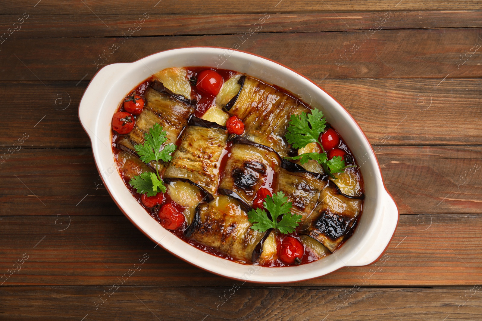 Photo of Tasty eggplant rolls with tomatoes, cheese and parsley in baking dish on wooden table, top view
