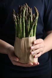 Photo of Woman with fresh asparagus on black background, closeup