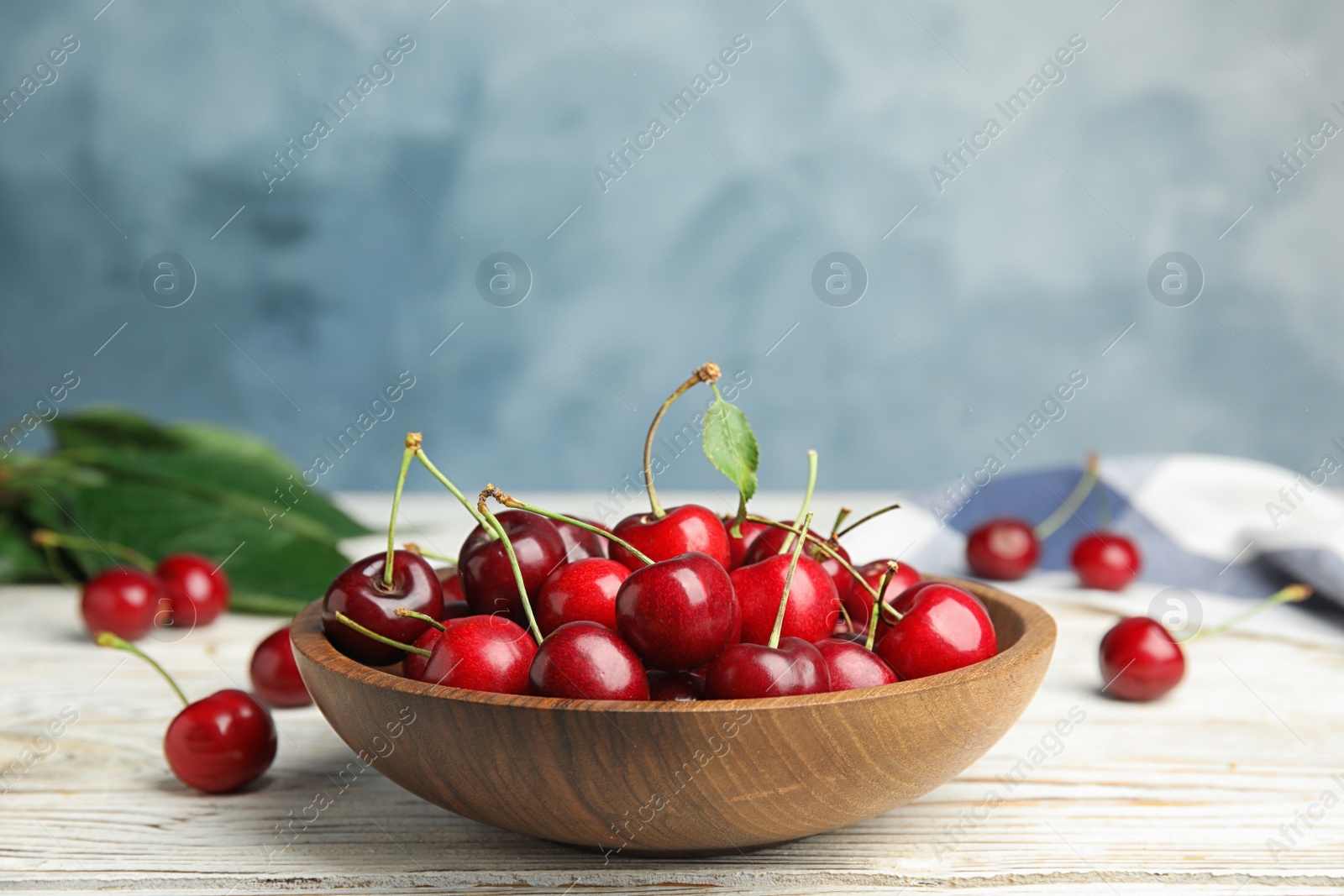 Photo of Bowl with ripe sweet cherries on white wooden table, space for text