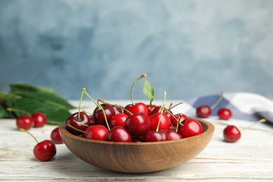 Photo of Bowl with ripe sweet cherries on white wooden table, space for text