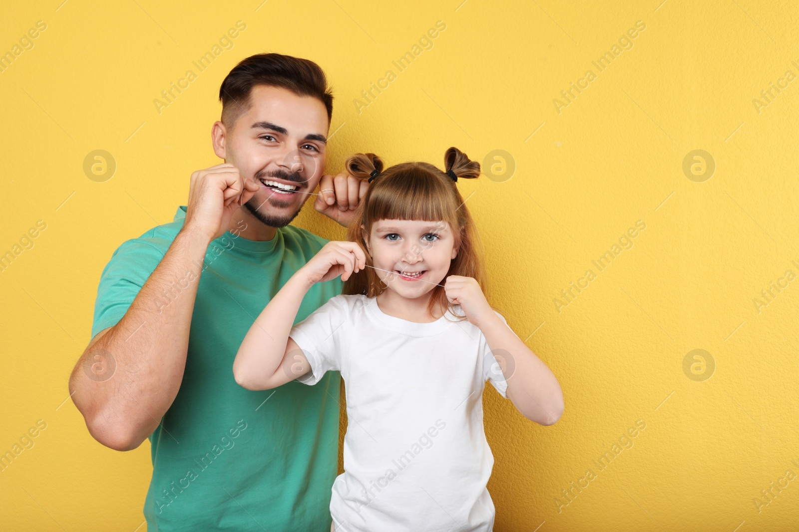 Photo of Little girl and her father flossing teeth on color background, space for text