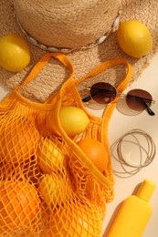 Photo of String bag with sunglasses, fruits and summer accessories on beige background, flat lay