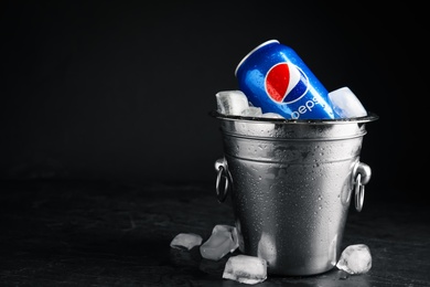 Photo of MYKOLAIV, UKRAINE - FEBRUARY 11, 2021: Can of Pepsi and ice cubes in bucket on black table against dark background, space for text