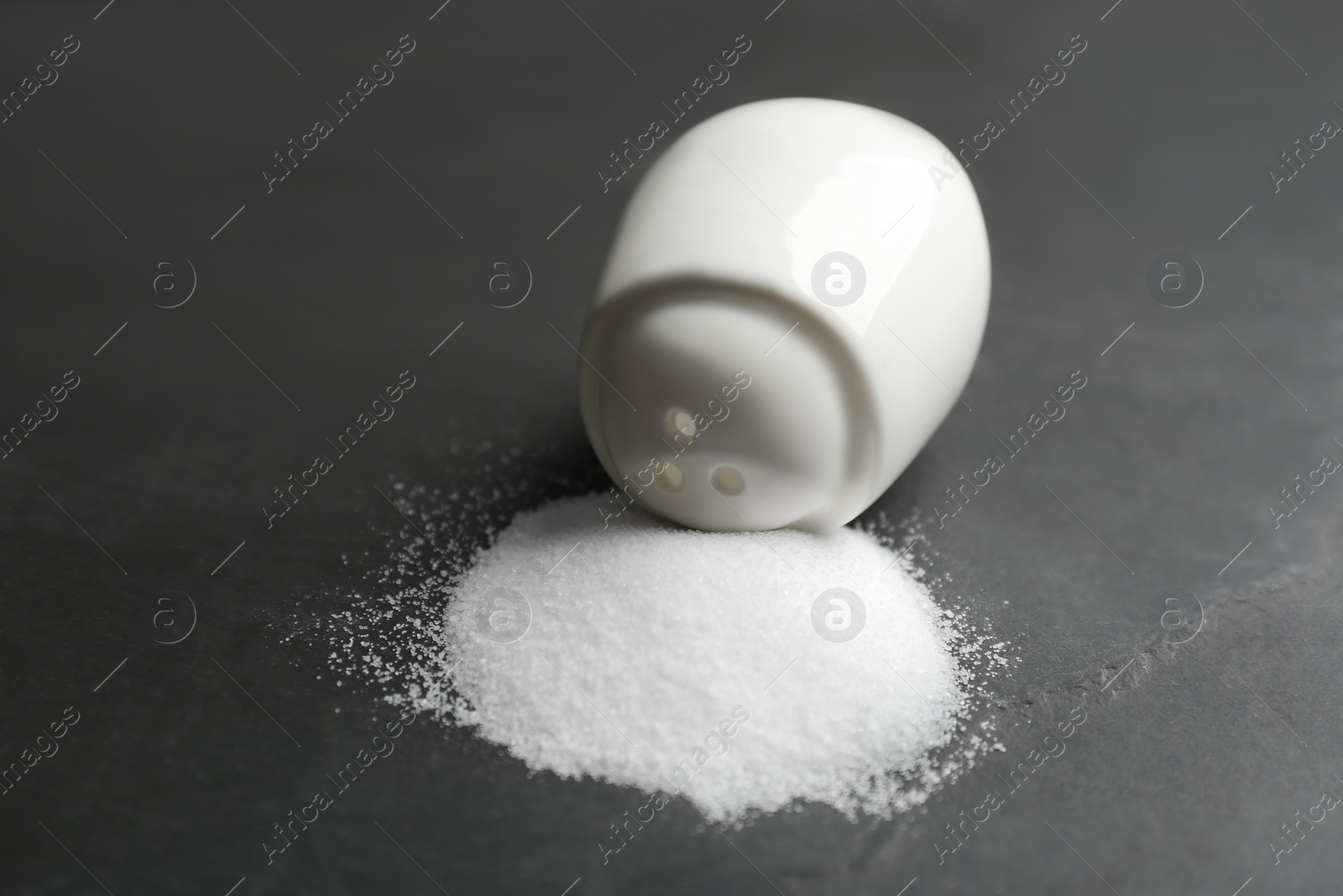 Photo of Scattered salt and shaker on black table, closeup