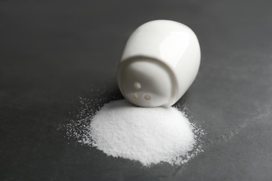 Photo of Scattered salt and shaker on black table, closeup