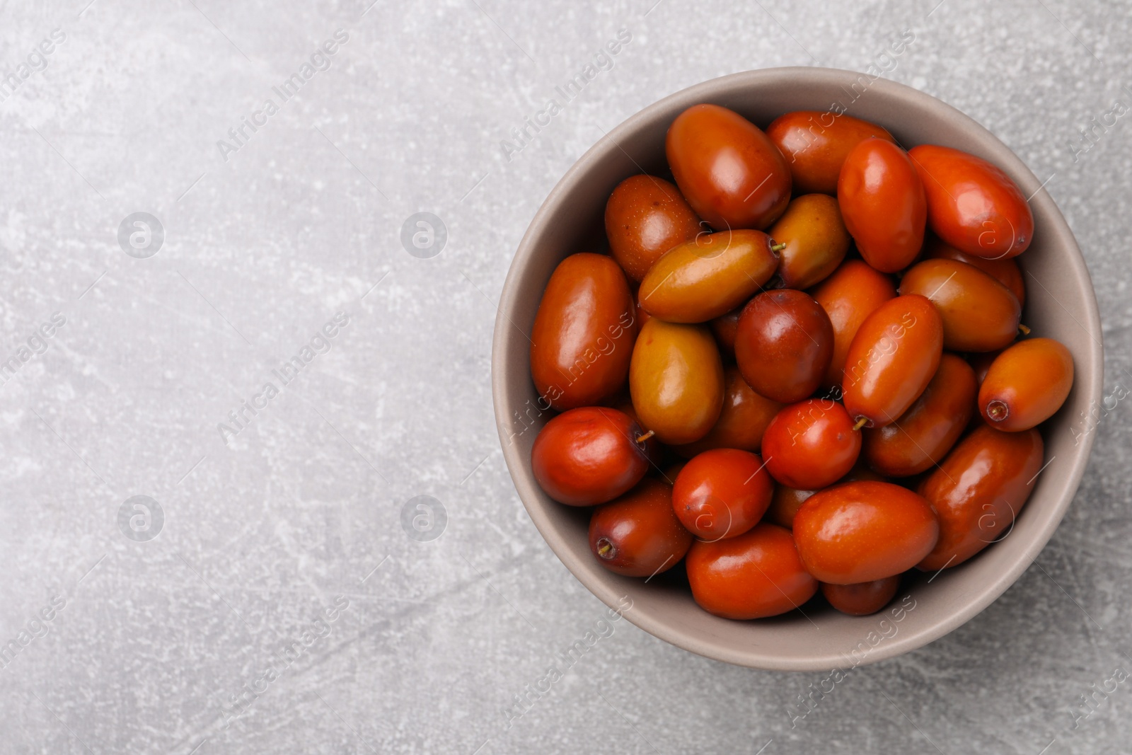 Photo of Fresh Ziziphus jujuba fruits in bowl on light table, top view. Space for text