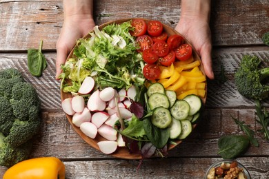 Photo of Vegetarian diet. Woman with plate of tasty vegetables at wooden table, top view