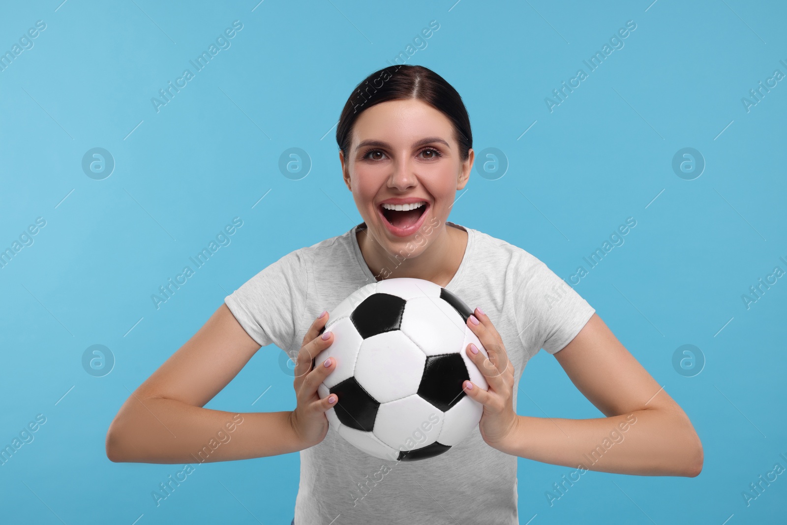 Photo of Emotional sports fan with soccer ball on light blue background