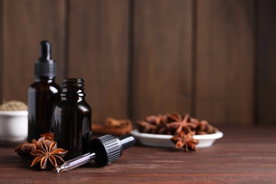 Anise essential oil and spice on wooden table, space for text