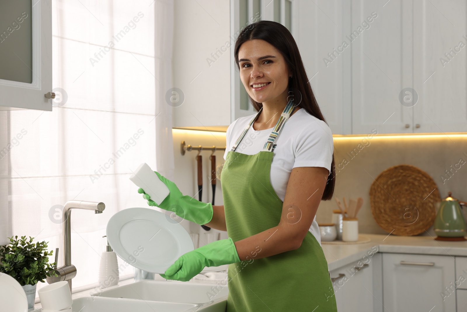 Photo of Happy woman washing plate at sink in kitchen