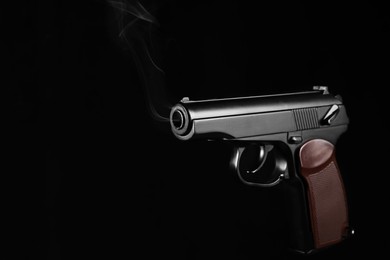 Photo of Handgun with smoke coming out of barrel on dark background, space for text
