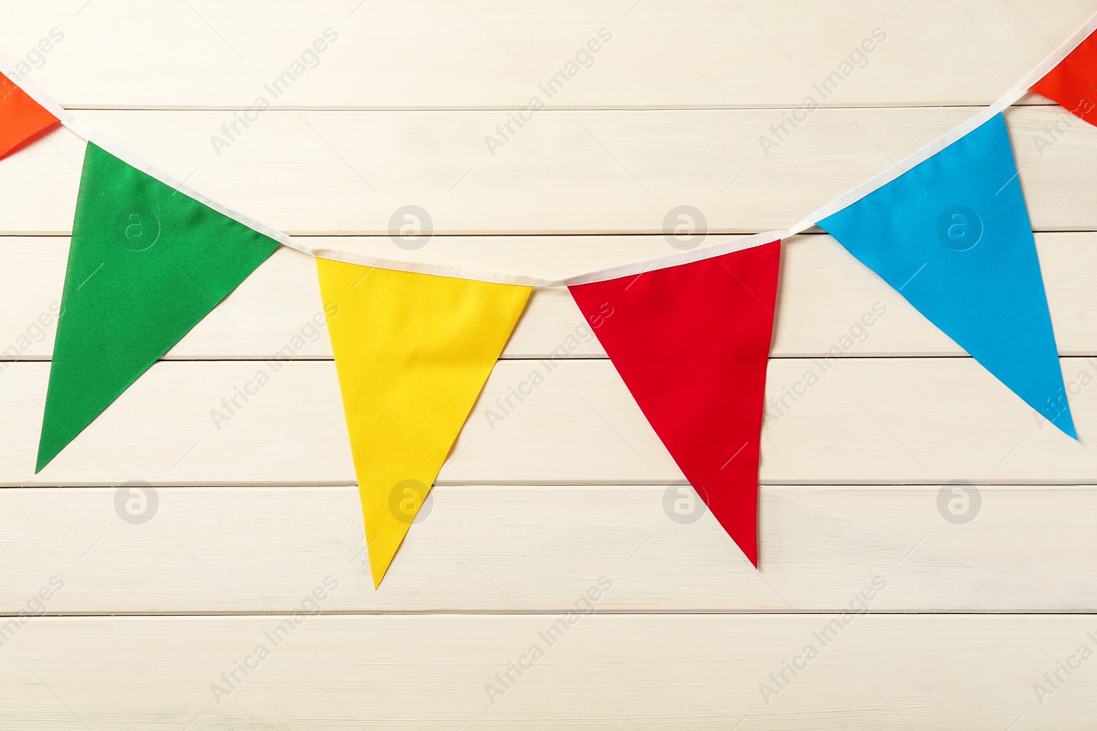 Photo of Bunting with colorful triangular flags on white wooden background. Festive decor