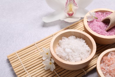 Photo of Different types of sea salt and flowers on light table, closeup. Spa products