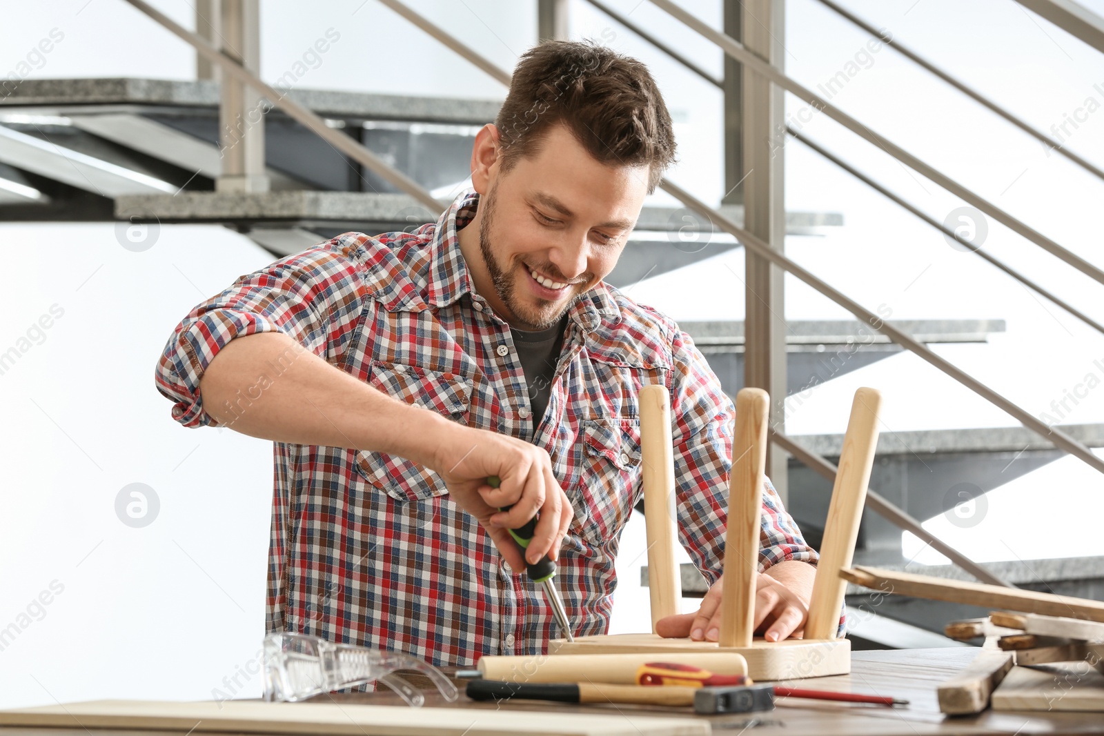 Photo of Handsome working man repairing wooden stool at table indoors