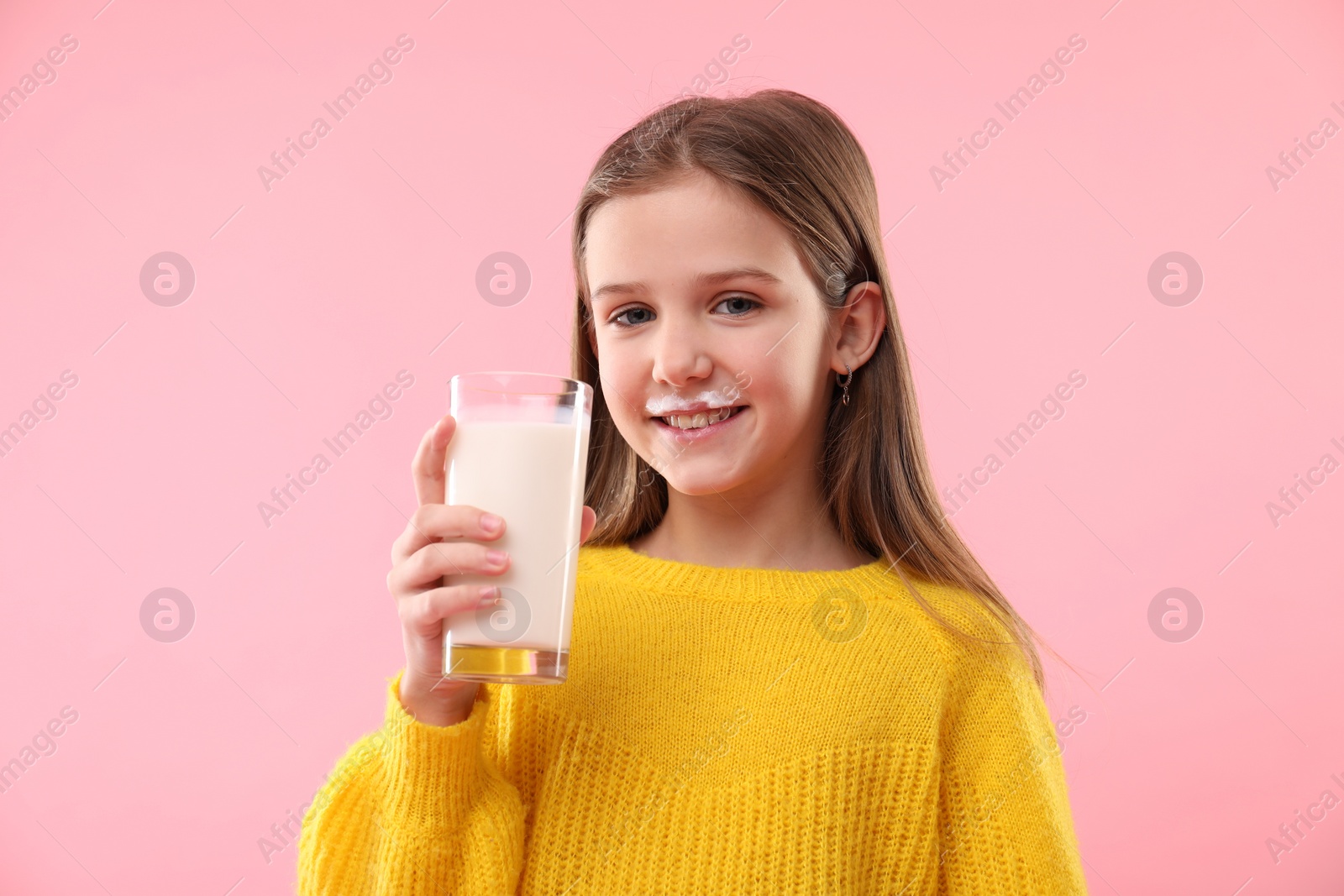 Photo of Happy little girl with milk mustache holding glass of tasty dairy drink on pink background