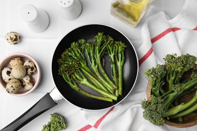 Photo of Frying pan with tasty cooked broccolini and other products on white tiled table, flat lay