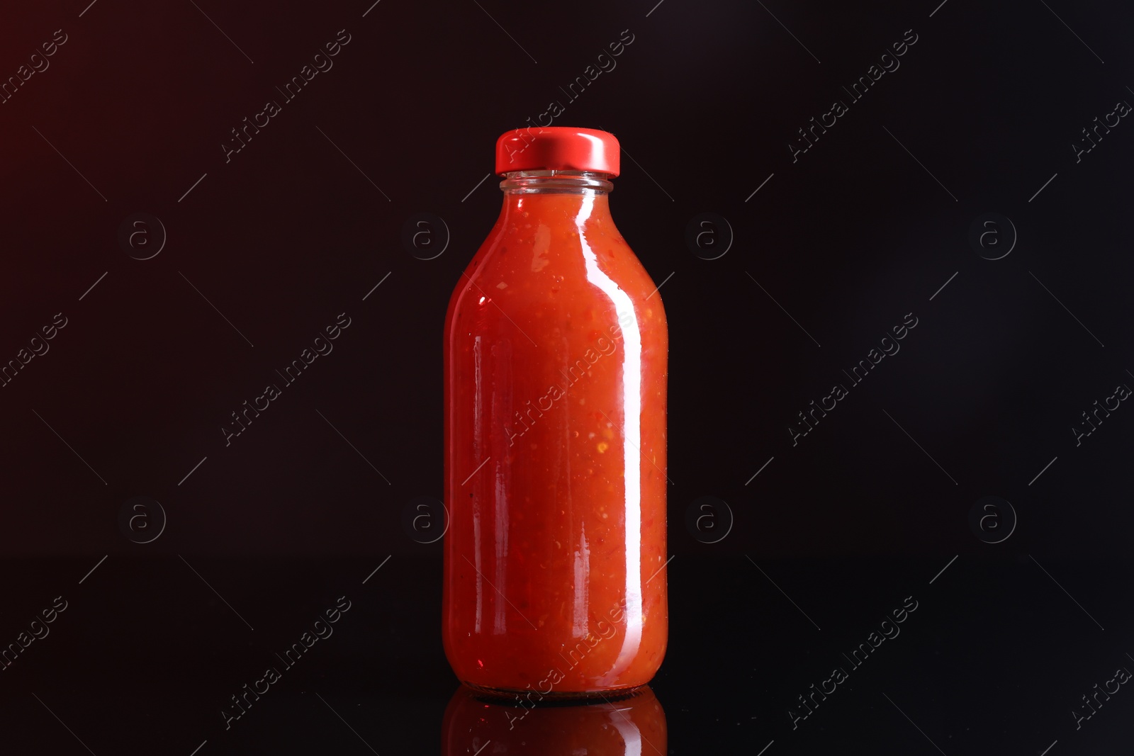 Photo of Spicy chili sauce in bottle on against dark background