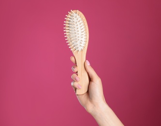 Woman holding wooden hair brush against crimson background, closeup. Space for text