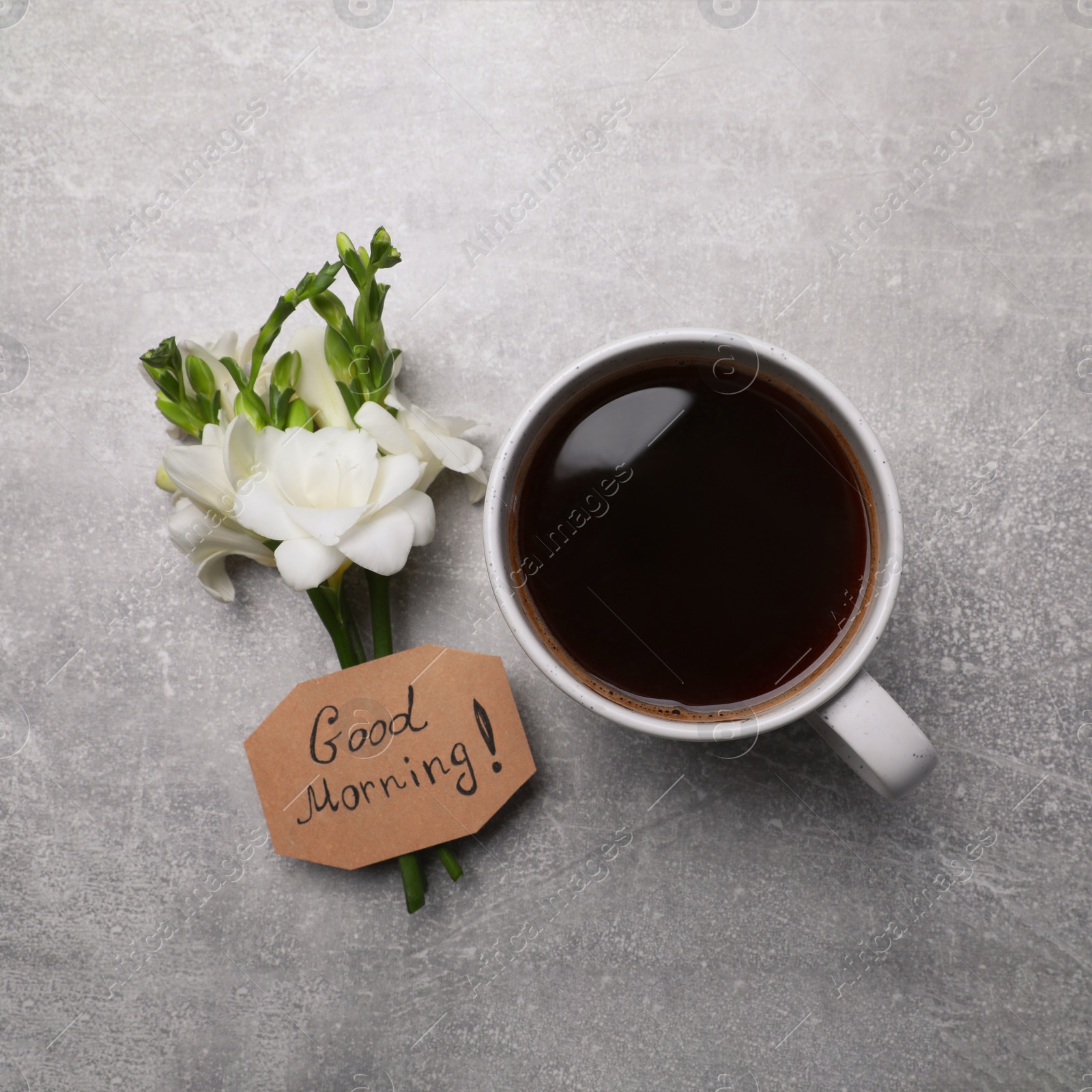 Photo of Aromatic coffee, flowers and Good Morning! message on light grey table, flat lay