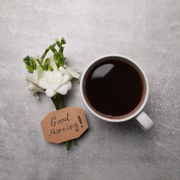 Aromatic coffee, flowers and Good Morning! message on light grey table, flat lay